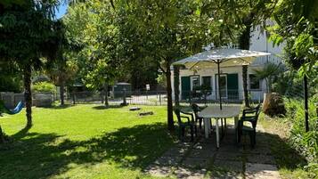 Eine Außenpatio mit Tisch und Stühlen, umgeben von Grünpflanzen und einem Zaun.