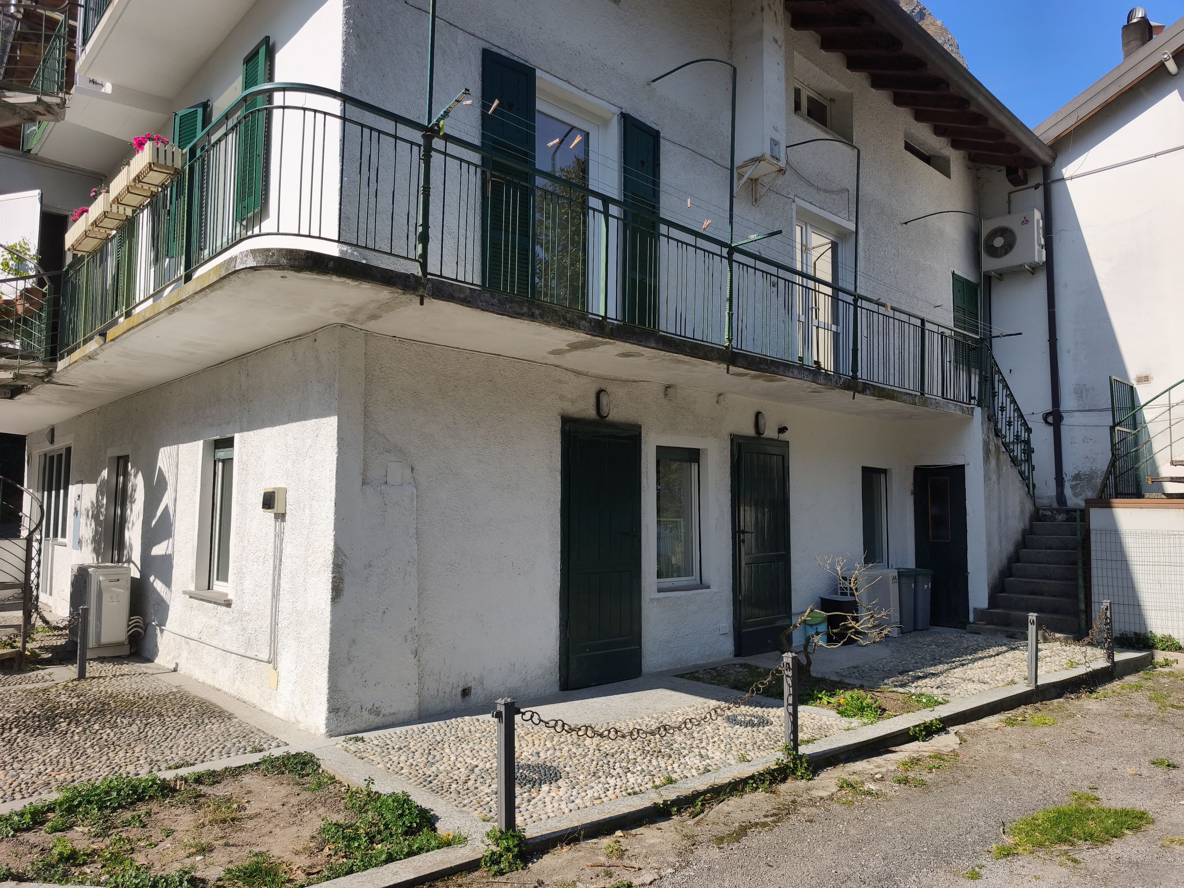 Ein zweistöckiges Gebäude mit einem Balkon, einer Treppe und einem kleinen Garten.