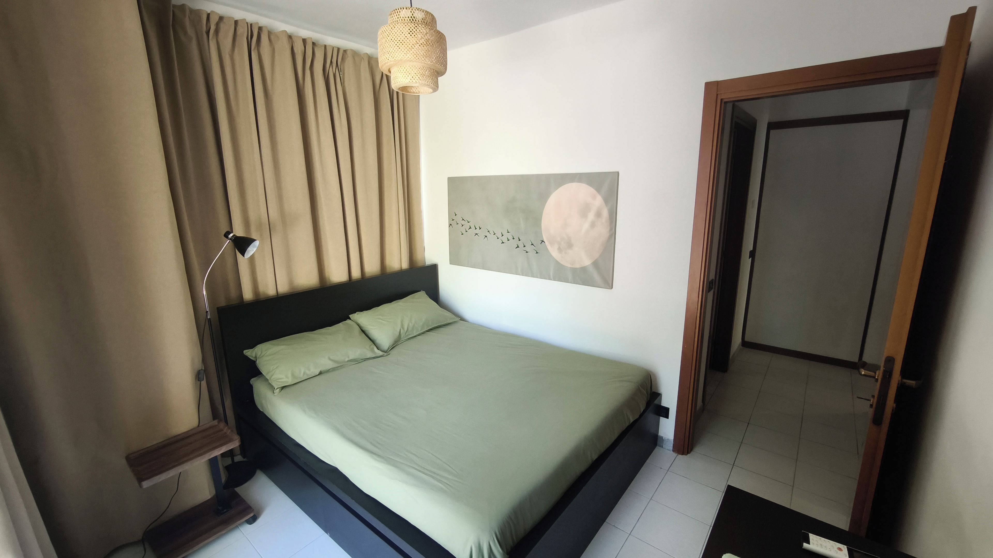 A bedroom with a bed, a bedside lamp, a wall-mounted artwork, and a door.