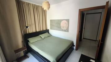 A bedroom with a bed, a bedside lamp, a wall-mounted artwork, and a door.