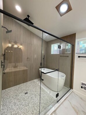 Un baño moderno con ducha acristalada, bañera independiente y suelo de baldosas.