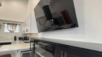A modern kitchen with a large flat-screen TV mounted on the wall, a built-in oven, and a microwave.