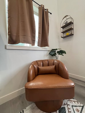 Una silla de cuero marrón en una habitación con una ventana, una planta y un estante fijado a la pared.