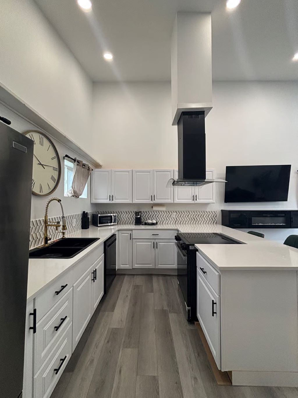A modern kitchen with white cabinetry, a built-in microwave, and a large clock on the wall.