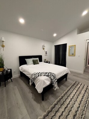 Een moderne slaapkamer met een groot bed, nachtkastjes, een vloerlamp en een vloerkleed.