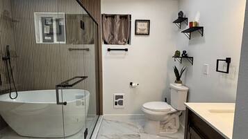 A modern bathroom with a glass-enclosed shower, a freestanding bathtub, a toilet, and a vanity with a mirror.