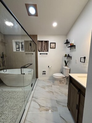 Een moderne badkamer met een douchecabine, een vrijstaand bad, toilet en een wastafel met spiegel.