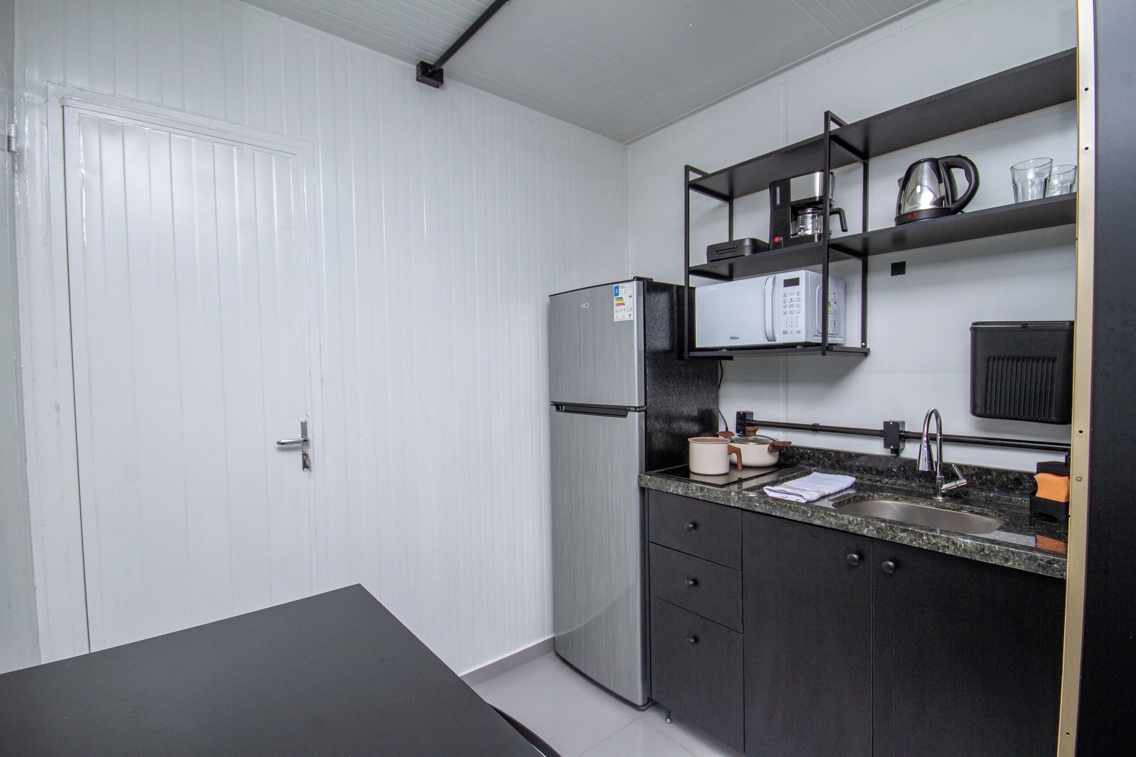 A compact kitchenette with a refrigerator, microwave, and a coffee maker on a shelf.