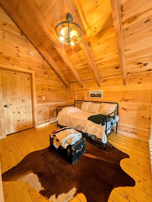 A cozy cabin room with a bed, a wooden ceiling, and a ceiling light fixture.