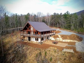 A log cabin with a covered porch, a stone fireplace, and a dirt driveway.