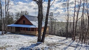 A cabin with a porch, surrounded by trees and snow.
