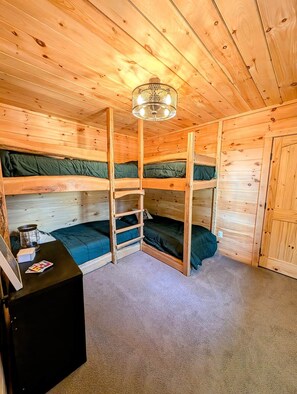 A wooden cabin with bunk beds, a desk, and a chandelier.