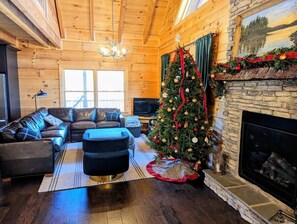 A cozy living room with a fireplace, a Christmas tree, and a stone wall.