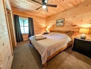 A wooden cabin bedroom with a bed, a ceiling fan, a nightstand, and a dresser.