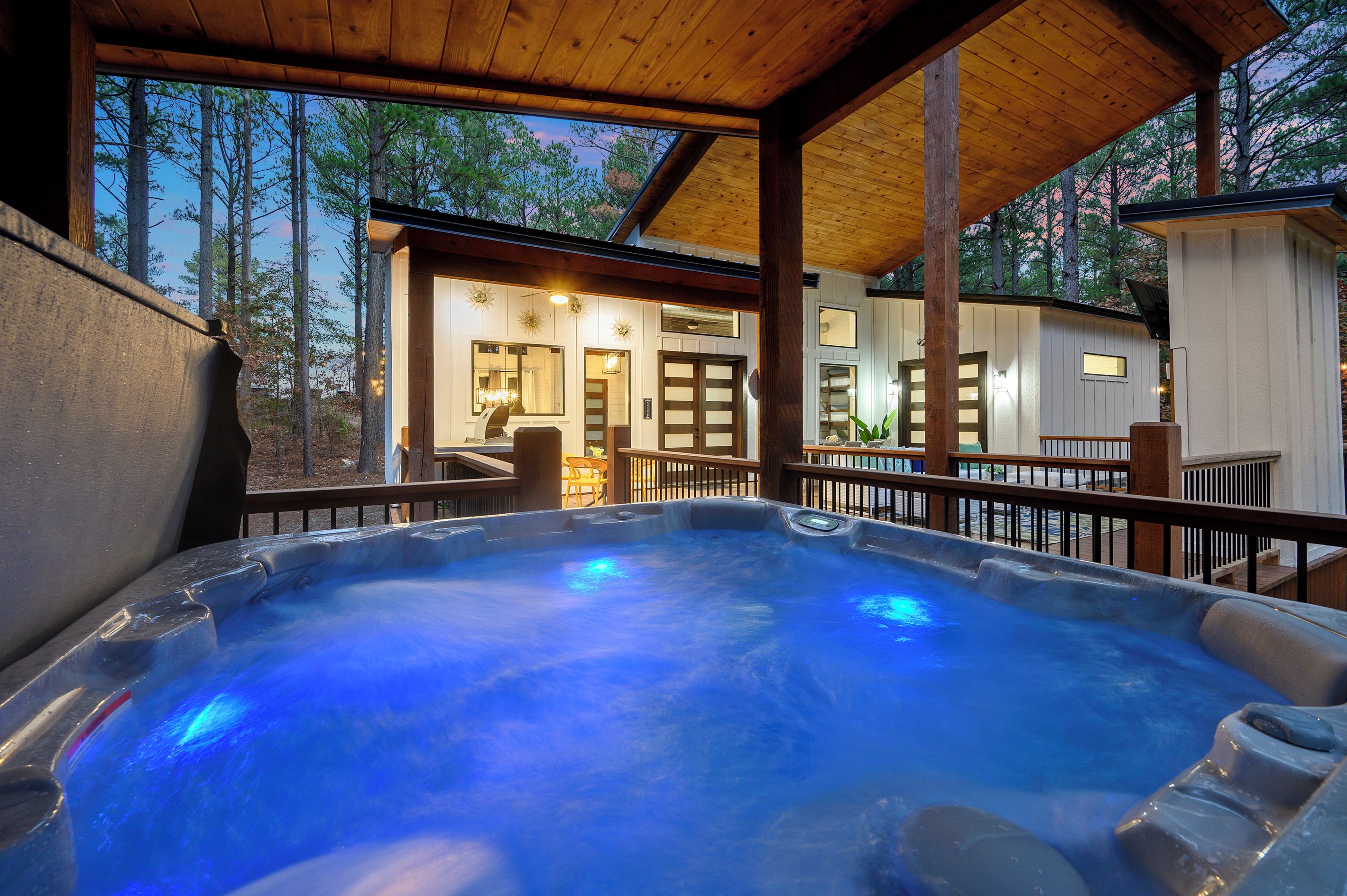Un bain à remous avec une terrasse en bois et vue sur un chalet doté d’un porche.