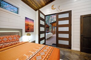 A bedroom with a bed, a nightstand, a lamp, and a view of a deck and trees through an open door. - Large Deck! Hot tub! HorseShoe Set! Outdoor Dining (Broken Bow)