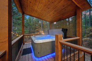 A wooden deck with a hot tub, surrounded by trees and a wooden railing. - Large Deck! Hot tub! HorseShoe Set! Outdoor Dining (Broken Bow)