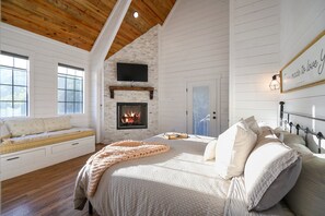 Ein Schlafzimmer mit Kamin, einem Bett mit Kissen, einem Fenster und einem an der Wand montierten Fernseher.