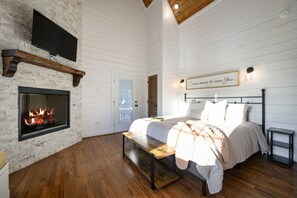 Quarto com lareira, cama, um banquinho e luminária fixada na parede.