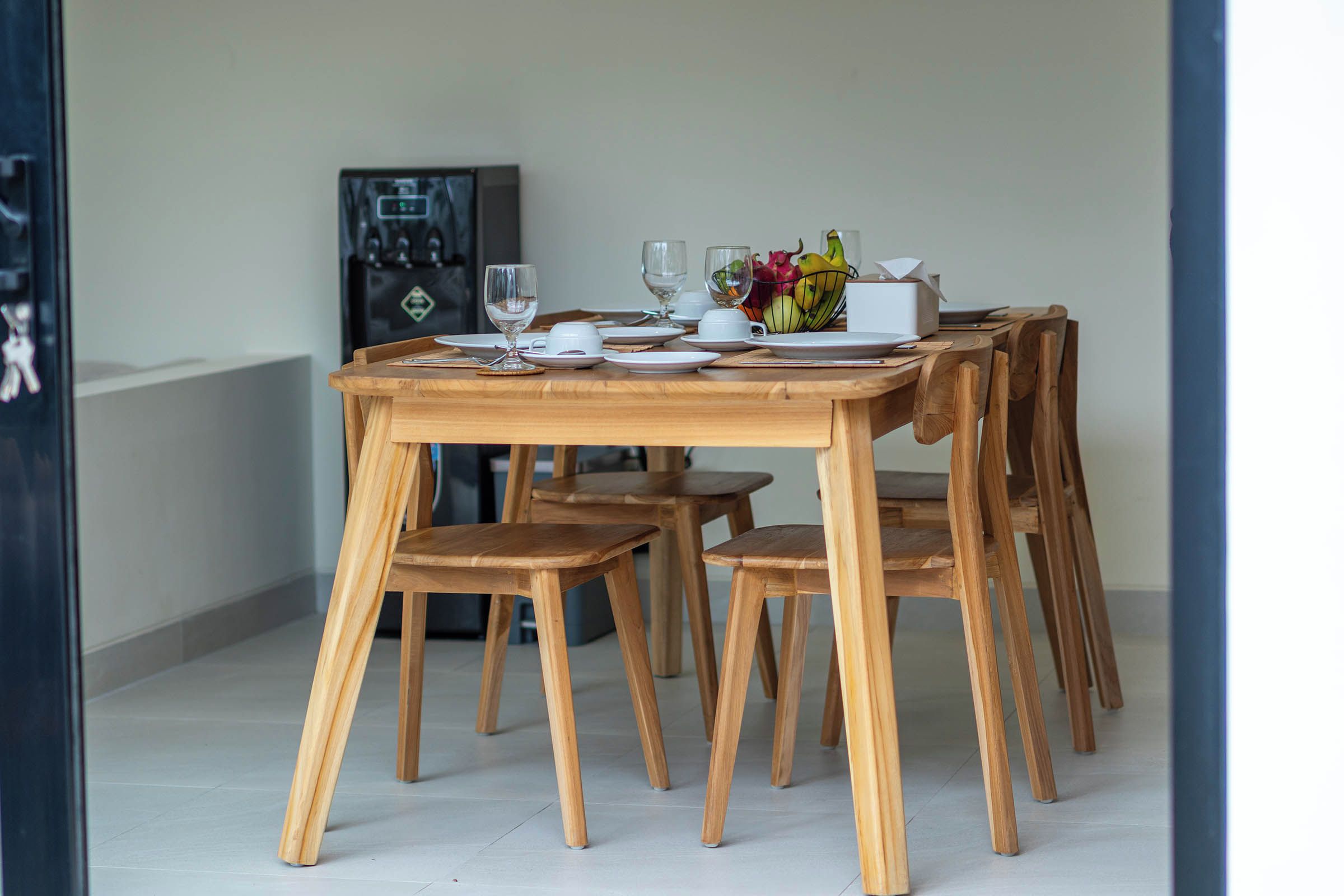 Une table à manger avec des chaises, des assiettes, des verres et un saladier rempli de fruits.