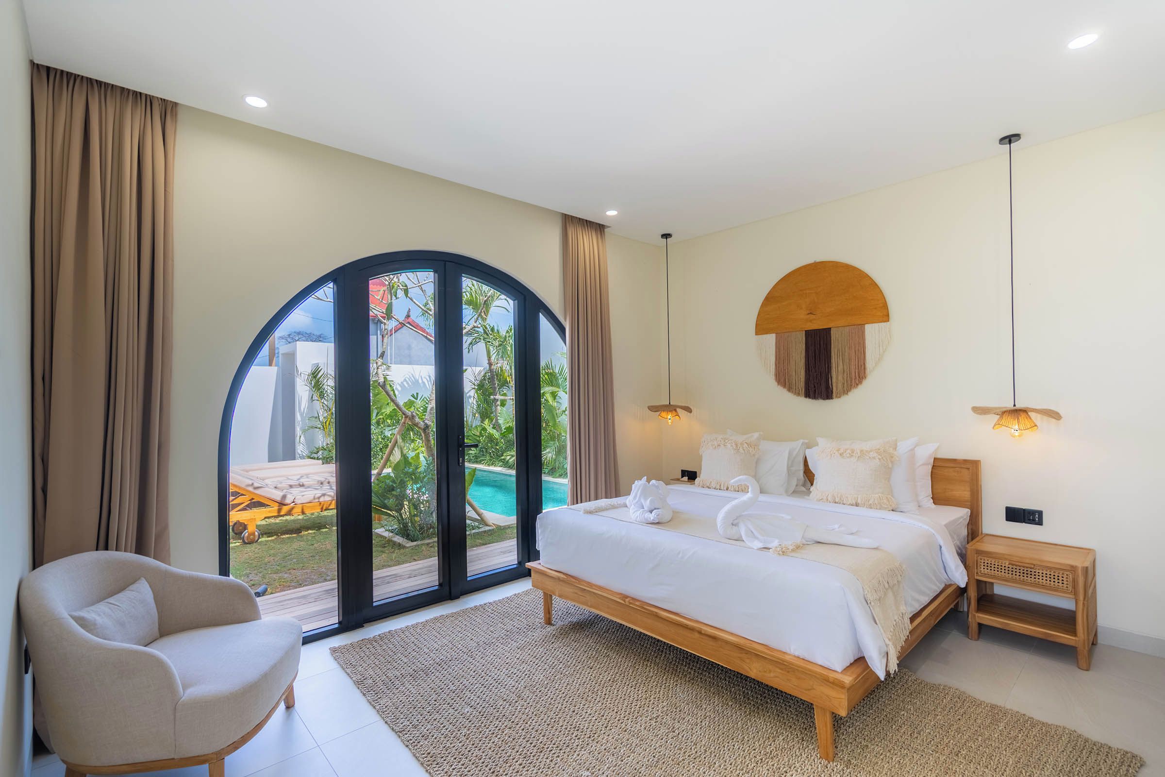 Quarto com cama, uma cadeira, vista para piscina externa e detalhe de teto de madeira.