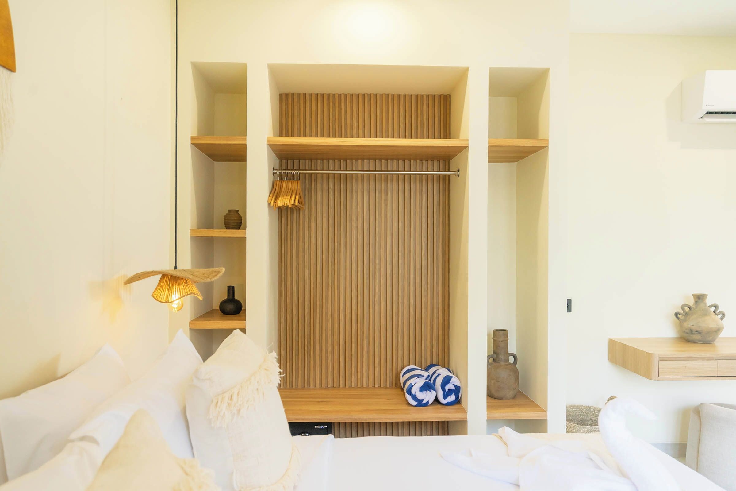 A bedroom with a bed, a bedside table, a wall-mounted shelf, a hanging light, and a wooden panel wall.