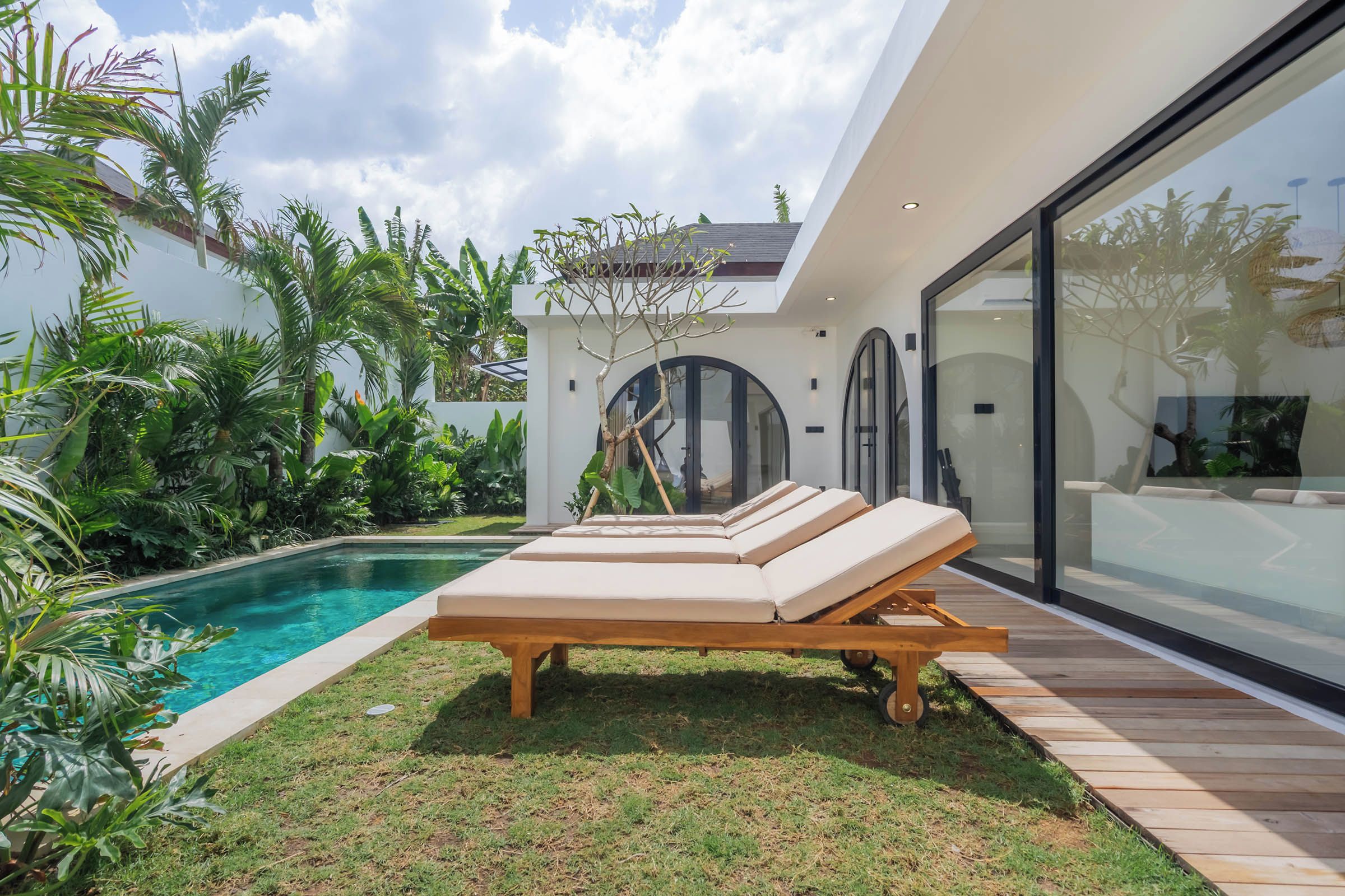 Un espace piscine extérieur moderne, doté de chaises longues et de plantes tropicales.