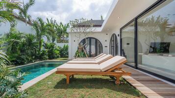 Un espace piscine extérieur moderne, doté de chaises longues et de plantes tropicales.