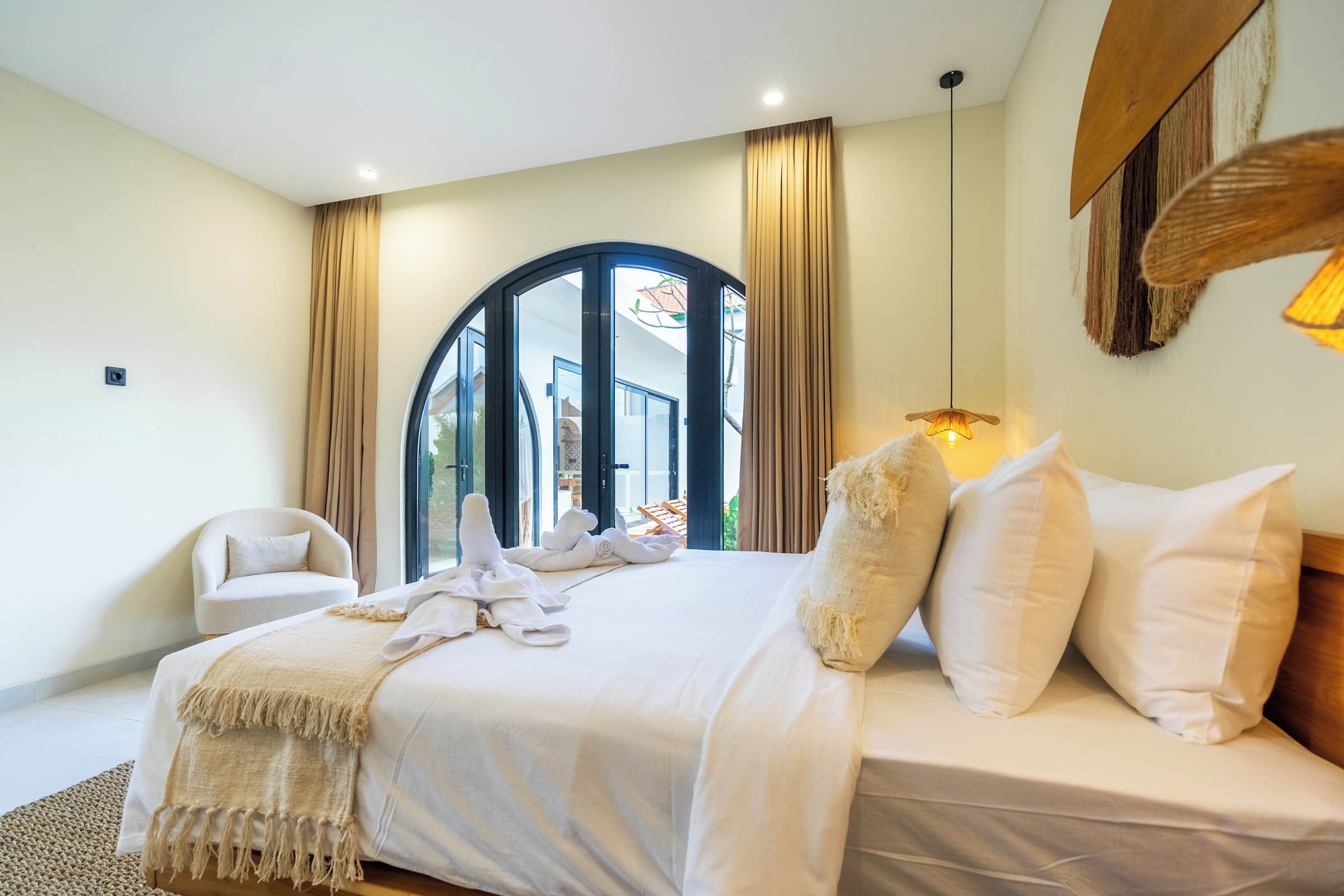 A bedroom with a bed, a chair, a large window, and a view of the outside.
