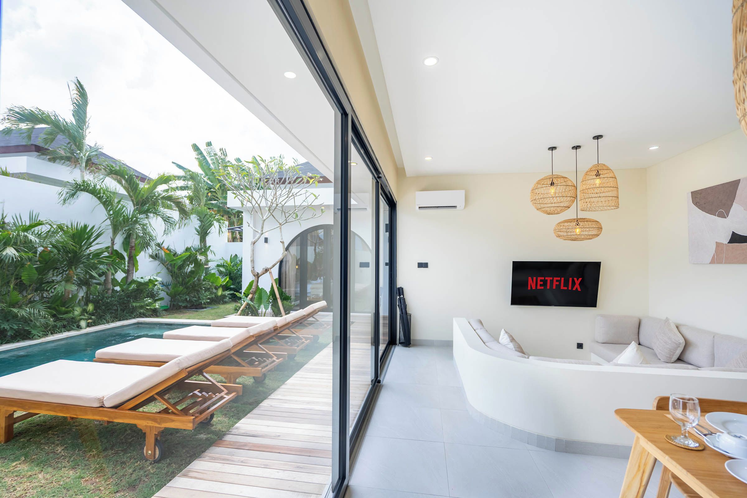 Un salon moderne doté d’un canapé incurvé, d’un téléviseur à écran plat et d’un espace piscine avec des chaises longues.