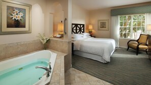 Ein Hotelzimmer mit einer großen Badewanne, einem Bett mit weißer Bettwäsche, einem Sessel und einem Fenster mit Blick auf Bäume.