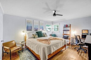 Ein Schlafzimmer mit einem Bett, einem Schreibtisch, einem Stuhl, einem Bücherregal und einem Deckenventilator.