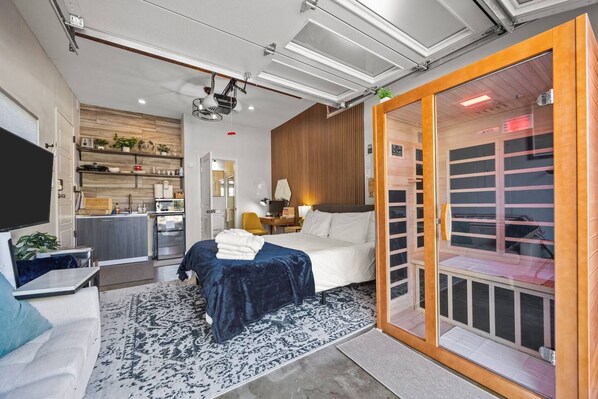 A modern hotel room with a bed, a desk, a television, and a sliding door leading to a bathroom.