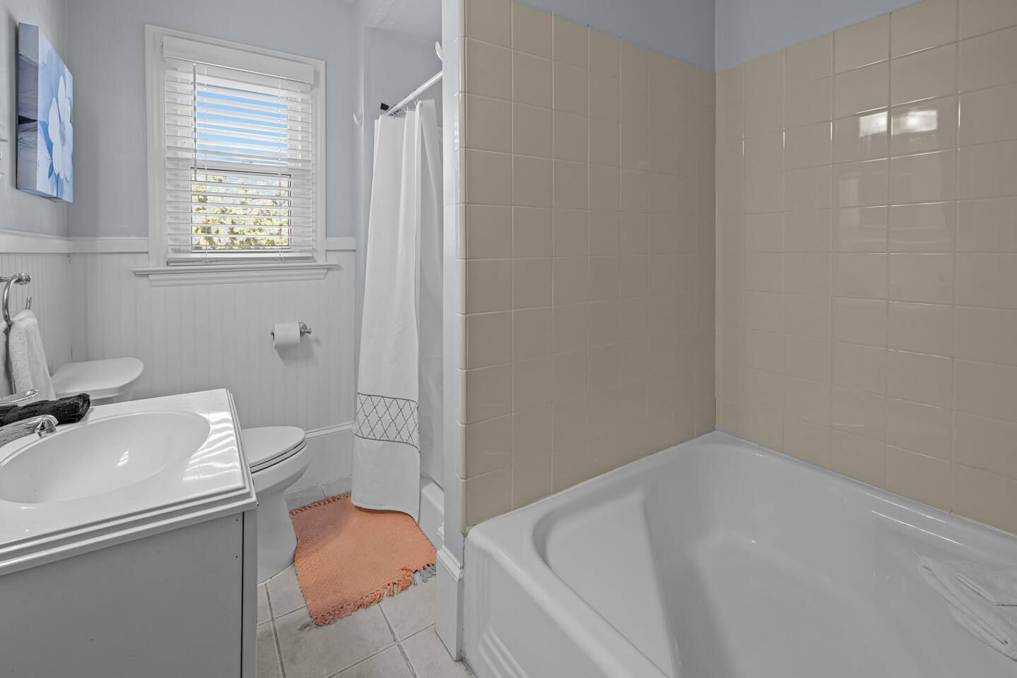 A bathroom with a bathtub, a sink, a toilet, and a window with blinds.