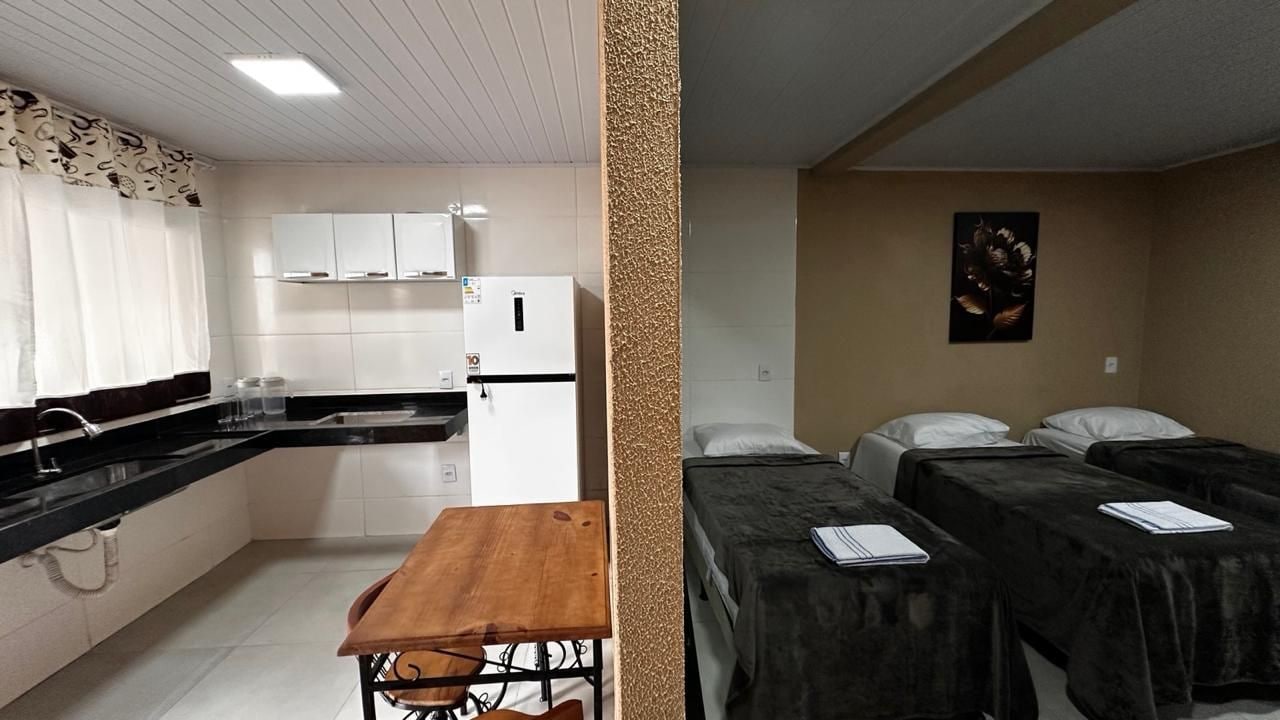 A room with a bed, bedside tables, a small table, and a kitchenette.