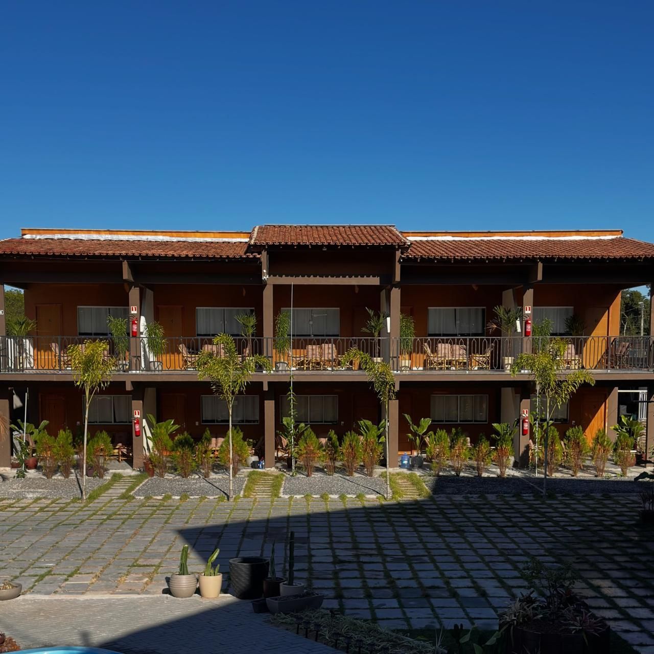 Un hotel de dos pisos, con mobiliario exterior y un patio empedrado.