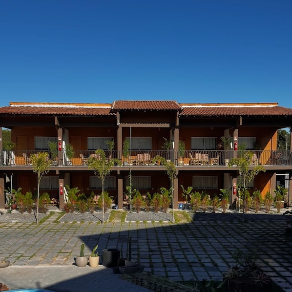 Un hotel de dos pisos, con mobiliario exterior y un patio empedrado.