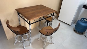 A small dining area with a wooden table and two chairs, a blue gas cylinder, and a white refrigerator. - MANDACARU POUSADA (Aracruz)