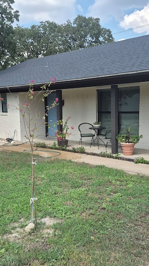 A residential building with a covered porch, a potted plant, a chair, and a small tree.
