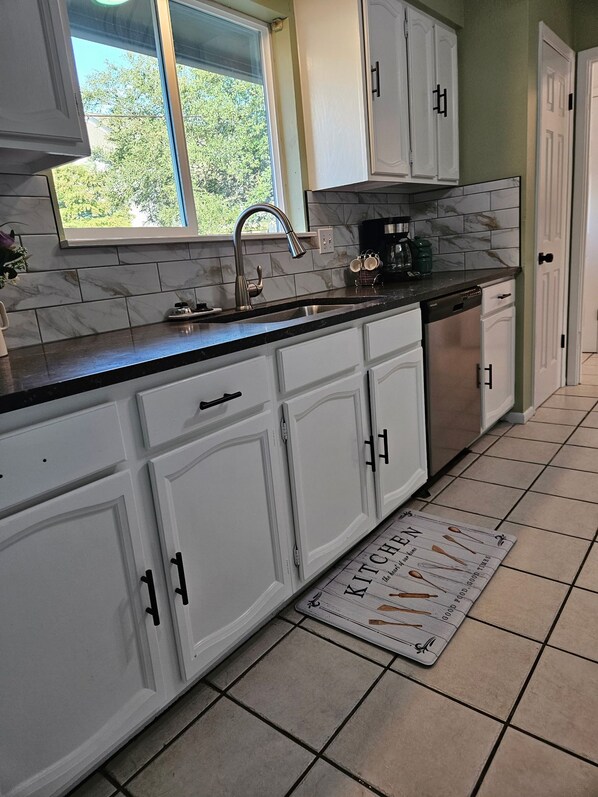 A kitchen with white cabinets, a stainless steel sink, a coffee maker, and a dish rack.