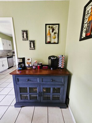 A kitchen counter with a coffee maker, a kettle, and a coffee mug. There are framed pictures on the wall above the counter.