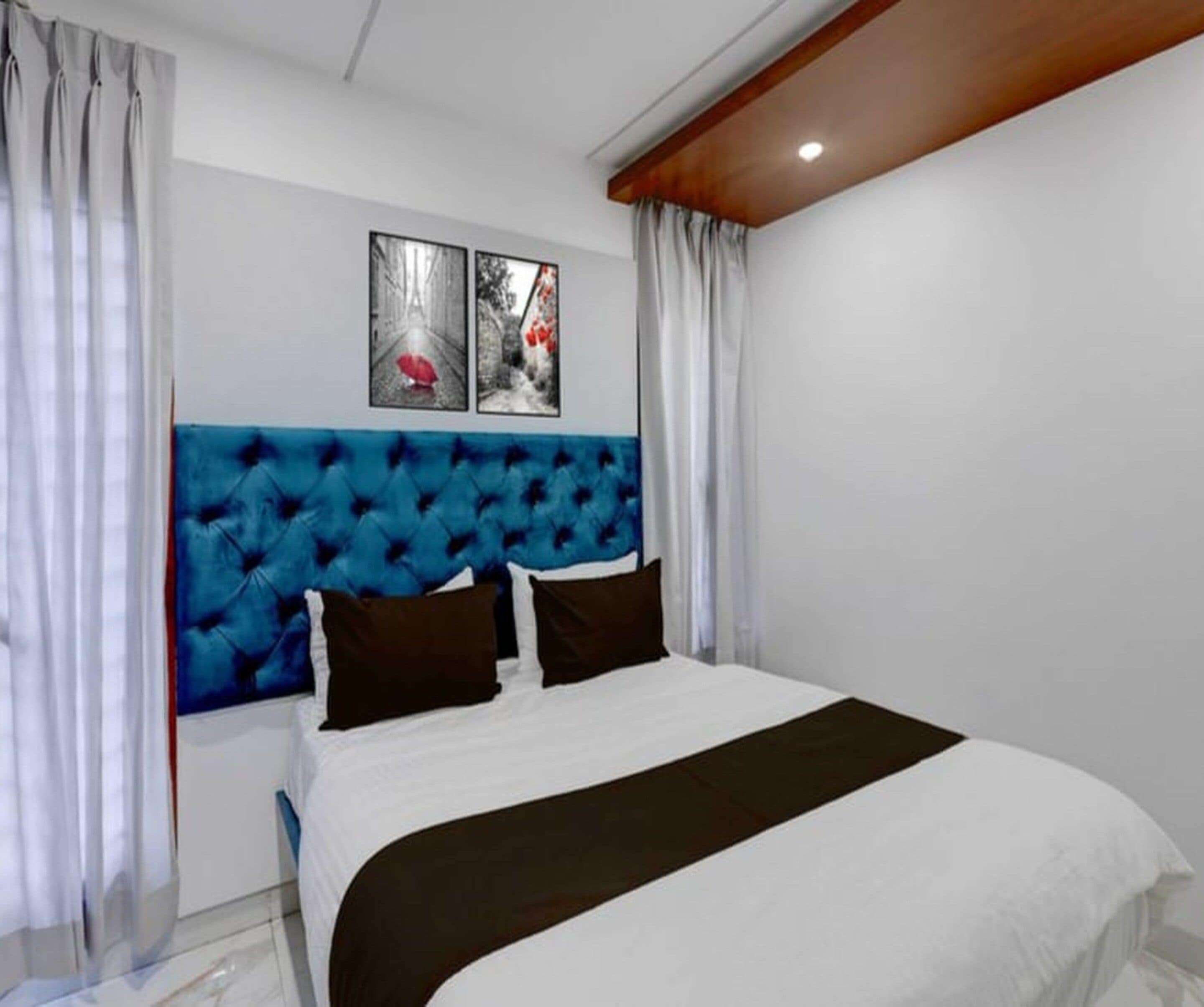 A bedroom with a tufted headboard, a bed with white and black bedding, and two framed pictures on the wall.