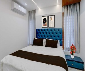 Una camera d'albergo moderna con un letto grande, una testiera blu e un condizionatore d'aria a parete.