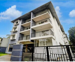 A multi-story residential building with balconies, a gated entrance, and a clear sky. - Deluxe Room Periyar Stay (Peermade)