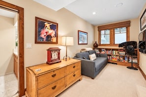A cozy living room with a wooden dresser, a grey sofa, a bookshelf, and a window with wooden shutters. - Beaver Creek True Ski-In/Ski-Out | Private Hot Tub (Beaver Creek)