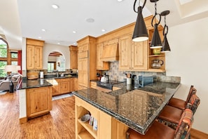 A modern kitchen with wooden cabinets, granite countertops, and a central island with seating. - Beaver Creek True Ski-In/Ski-Out | Private Hot Tub (Beaver Creek)