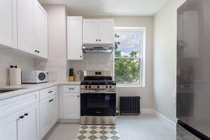 A kitchen with white cabinets, a stove, a microwave, and a window with a view of trees.