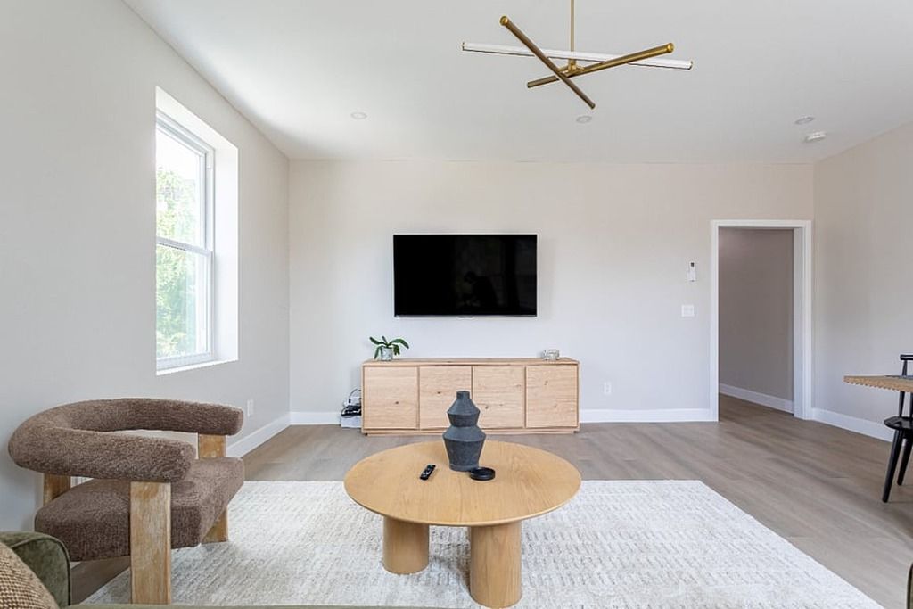 Uma sala de estar moderna com uma mesa de centro redonda de madeira, um arranhador para gatos, uma televisão fixada na parede e um armário de madeira minimalista.