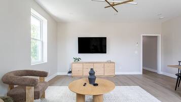 Uma sala de estar moderna com uma mesa de centro redonda de madeira, um arranhador para gatos, uma televisão fixada na parede e um armário de madeira minimalista.