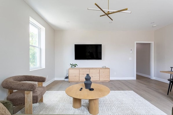 Uma sala de estar moderna com uma mesa de centro redonda de madeira, um arranhador para gatos, uma televisão fixada na parede e um armário de madeira minimalista.
